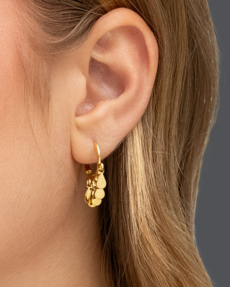 argola dourada Papoula banhada a ouro 18k com cinco gotas pendentes da coleção Lluvia usada pela modelo, semijoia feminina com movimento fluido e brilho delicado, fotografia aproximada destacando o caimento da argola, acabamento premium e estilo moderno