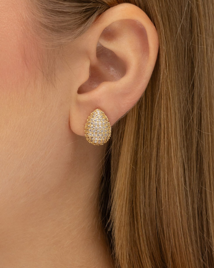 brinco de pressão dourado em formato de gota, cravejado de zircônias, semijoia Papoula com 1,5 cm por 1,0 cm, ideal para quem não tem orelha furada, fotografado em close