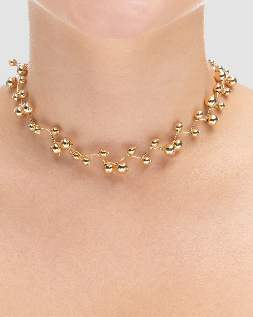 choker bolinhas dourada Papoula sendo usada por modelo, semijoia banhada a ouro 18k com design em bolinhas delicadas, 30cm + 15cm de ajuste, modelo com pele clara, blusa texturizada minimalista, estilo editorial premium, maquiagem natural elegante, fundo neutro cinza, fotografia de produto para e-commerce