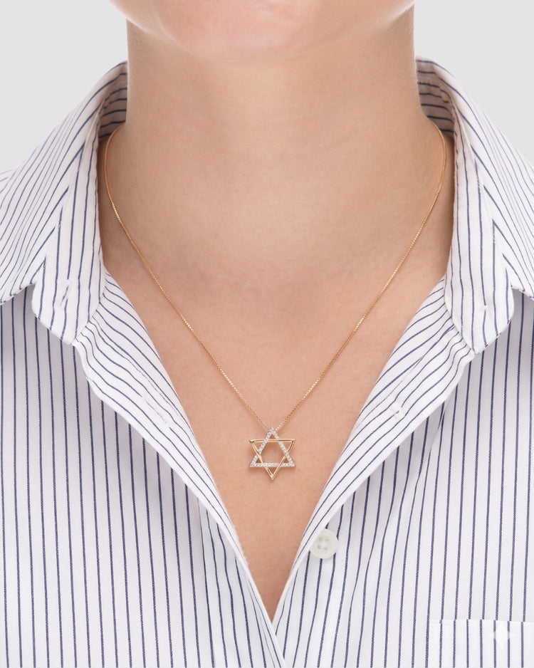 colar estrela de davi dourado Papoula sendo usado por modelo, semijoia banhada a ouro 18k com pendente estrela de 1,8cm em corrente veneziana de 45cm, zircônias brilhantes, modelo usando camisa branca com listras azuis, estilo editorial premium, fundo neutro cinza, fotografia de produto para e-commerce