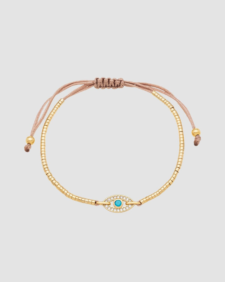 pulseira ajustável banhada a ouro 18k com pingente de olho grego com zircônia, semijoia feminina dourada exibida em close no pulso, fotografia em fundo claro com iluminação suave, acessório delicado de proteção e estilo