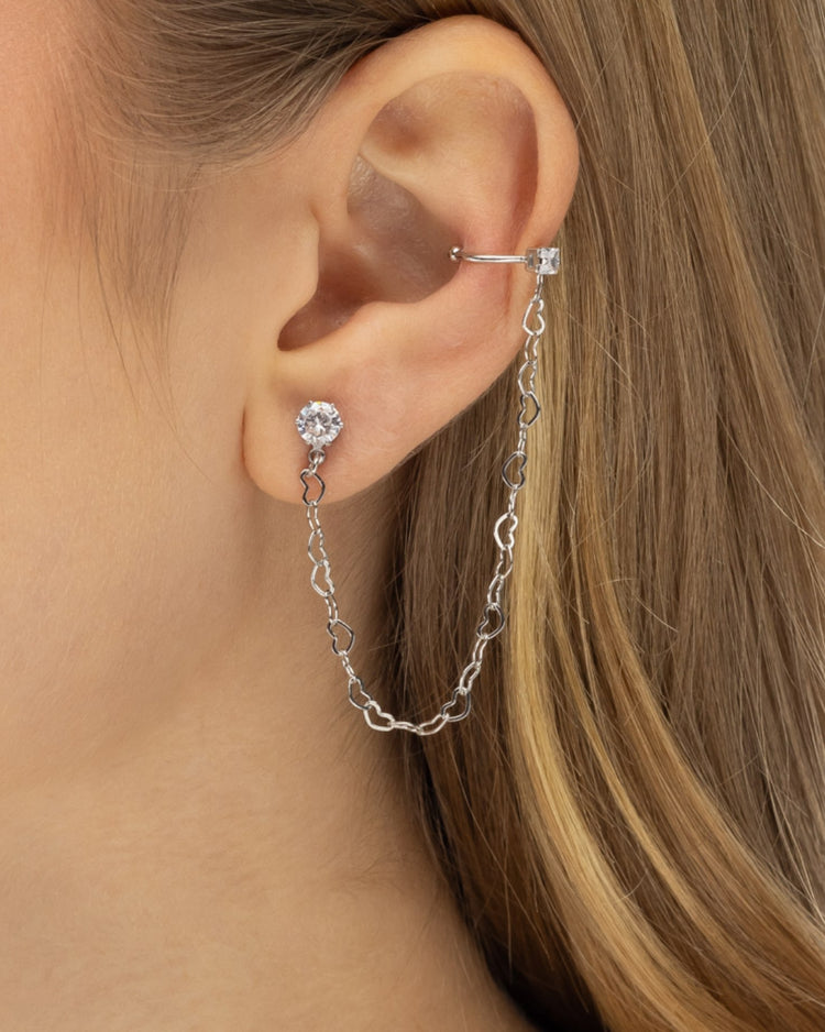 Modelo usando brinco ear line prateado com corrente elos coração zircônia e piercing fake ear cuff — semijoia feminina Papoula