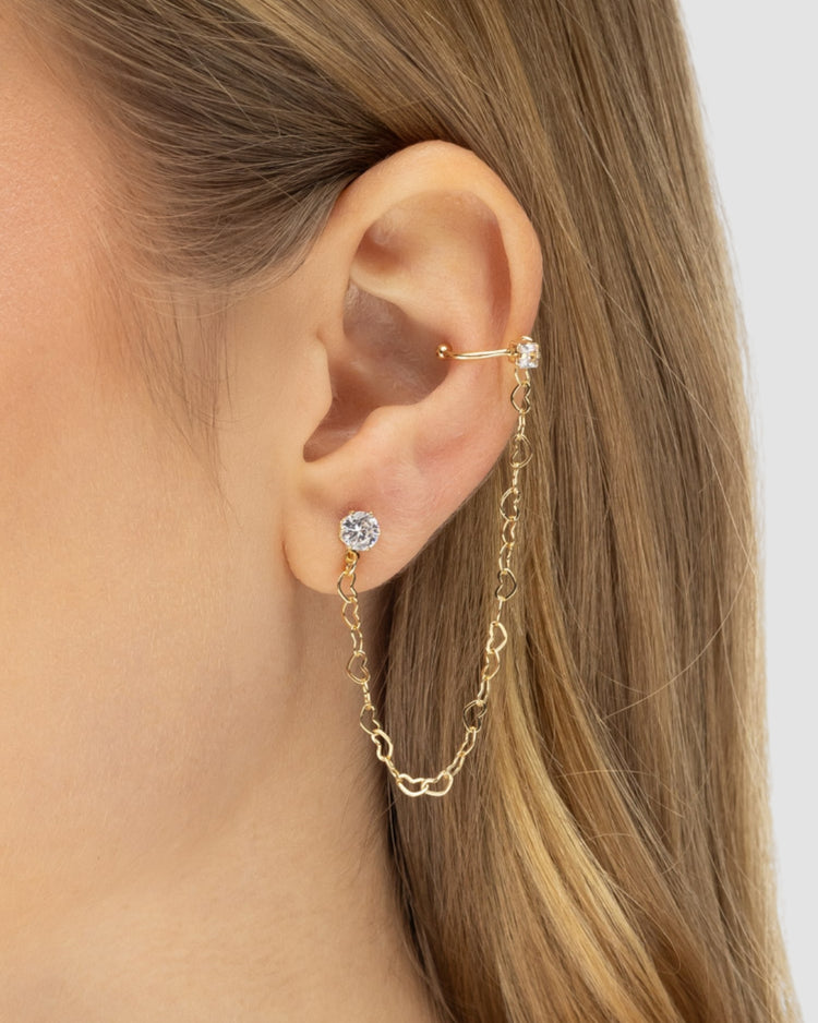 Modelo usando brinco ear line dourado com corrente elos coração zircônia e piercing fake ear cuff banhado a ouro — semijoia feminina Papoula