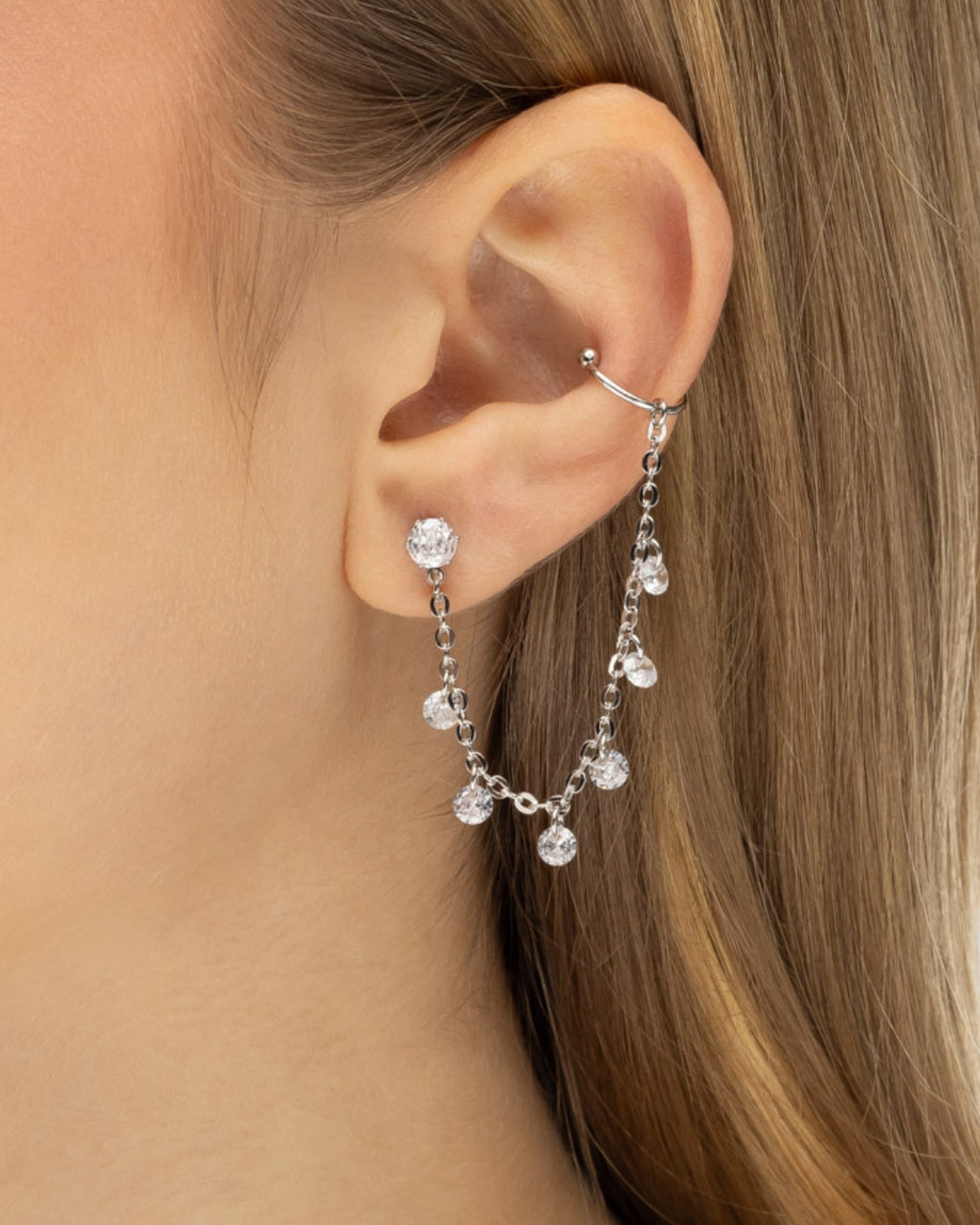 Modelo usando brinco ear line piercing fake prateado com zircônia e corrente ear stacking — semijoia feminina Papoula