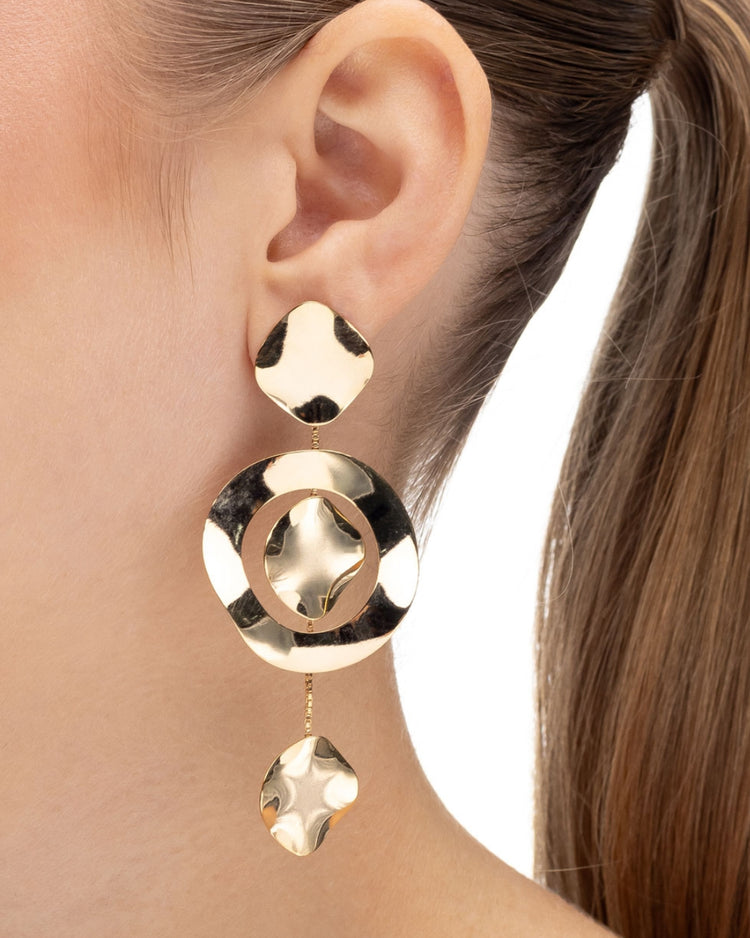 brinco movimento dourado Papoula com design em cascata, elementos orgânicos suspensos por correntes delicadas, 8,5 cm de comprimento e 3,5 cm de largura, semijoia com acabamento polido, fotografado na orelha