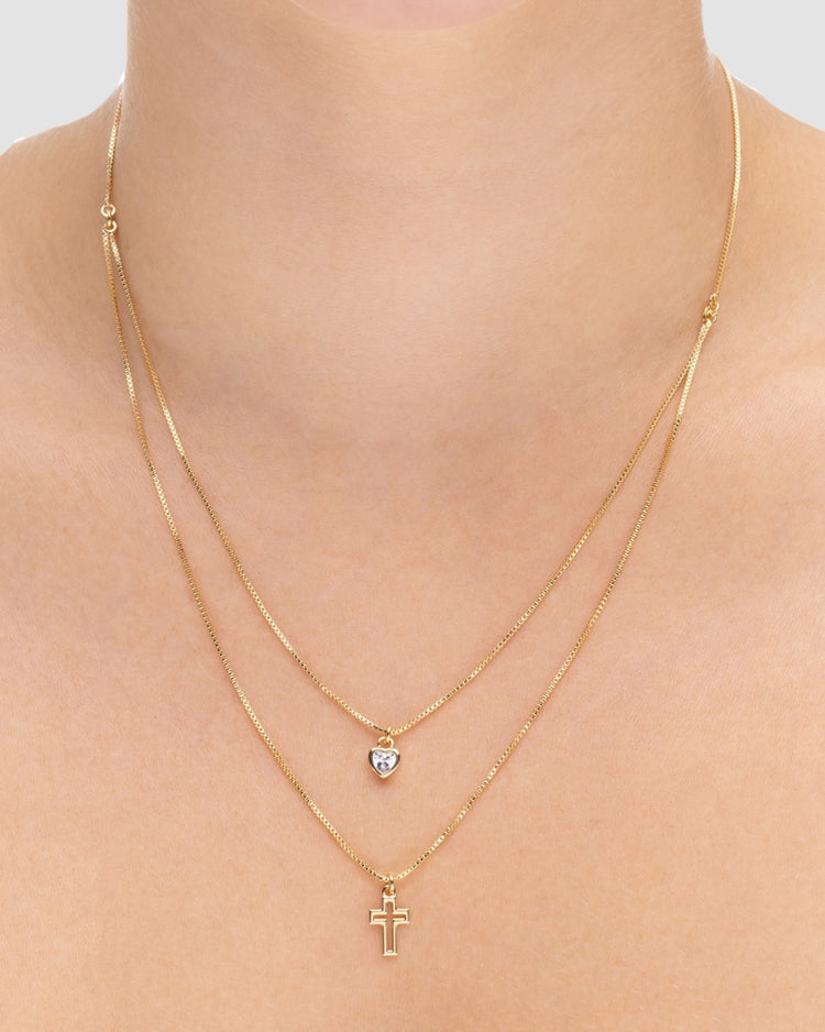colar duplo dourado Papoula, semijoia com duas correntes em camadas, pingente coração com zircônia e cruz vazada, corrente curta 42cm + 5cm extensão e corrente longa 46cm, acabamento polido, fotografado eno pescoço