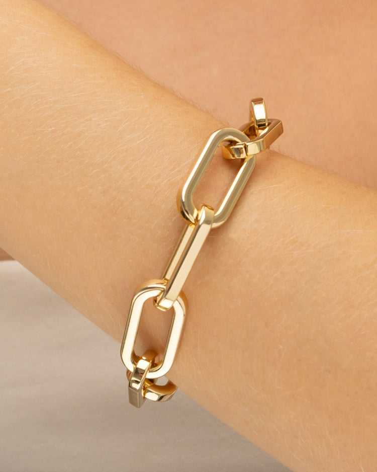 pulseira dourada de elos grossos em metal polido, estilo correntaria, semijoia Papoula, com banho de ouro 18k, destacada no pulso com acabamento brilhante em foto de close-up