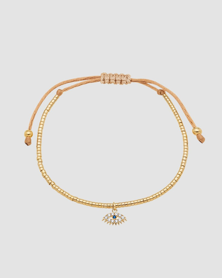 pulseira ajustável dourada com mini canutilhos e pingente de olho grego com zircônia, semijoia feminina banhada a ouro 18k exibida no pulso em fundo claro, fotografia detalhada com luz suave para destaque do acessório