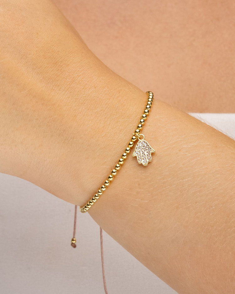 Pulseira ajustável dourada com pingente de hamsa cravejado no pulso, semijoia feminina banhada a ouro 18k, exibida em close sobre fundo claro.